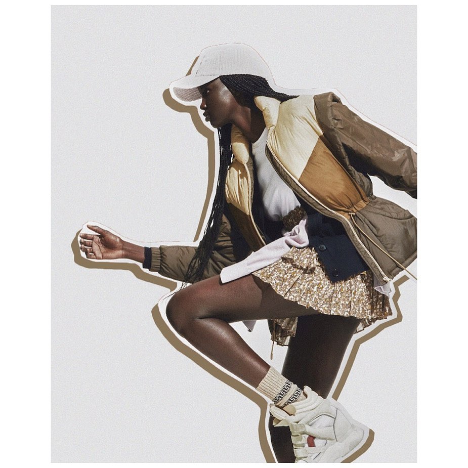Fashion portrait of a Black woman wearing a cap, puffer jacket, and gold skirt in a studio with a cutout effect and white background.