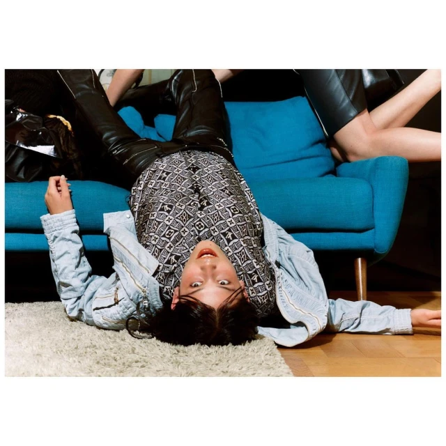 Upside down view of a person laying on a floor with a blue couch and a second person in the background.