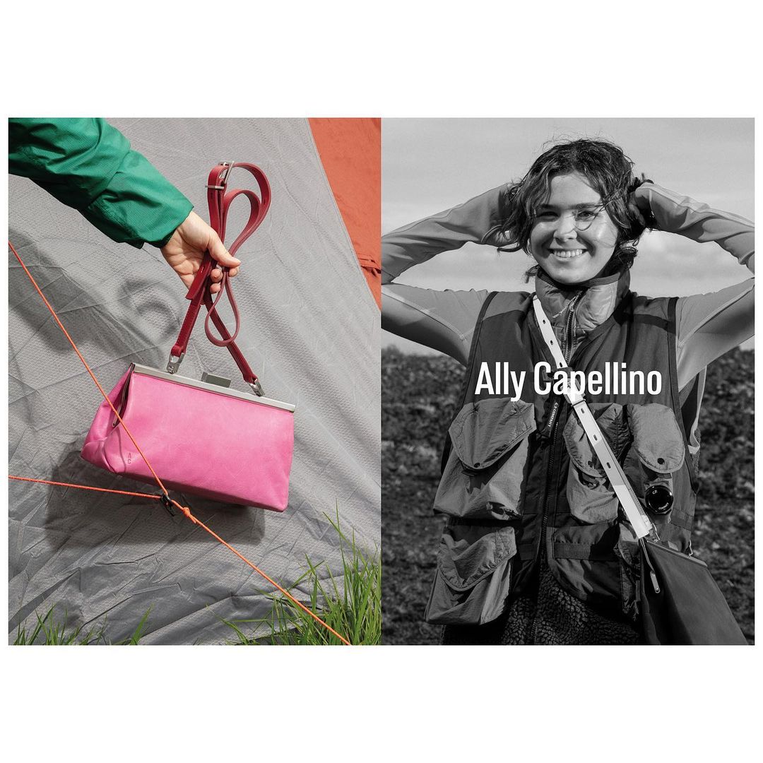 Pink leather purse with red straps held in hand near a tent wall and a person in a vest with Ally Capellino logo.