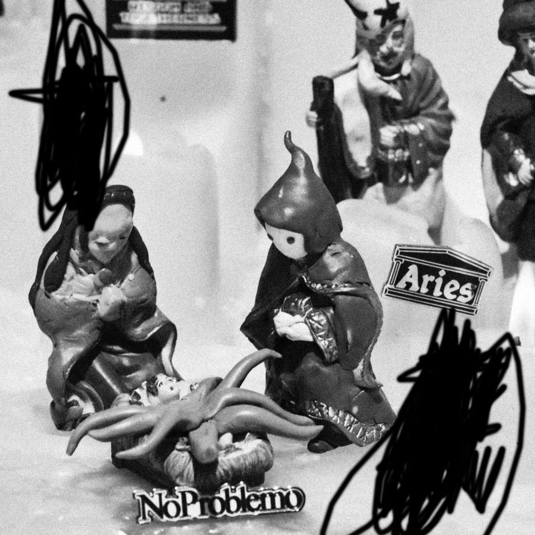 Black and white image of figurines arranged in a display, featuring religious figures and lettering. The scene is simply staged indoors.