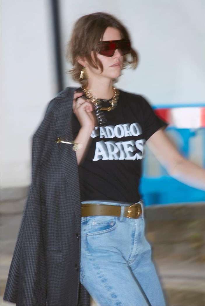 Woman wearing oversized tinted sunglasses, graphic t-shirt, and holding a patterned jacket over her shoulder