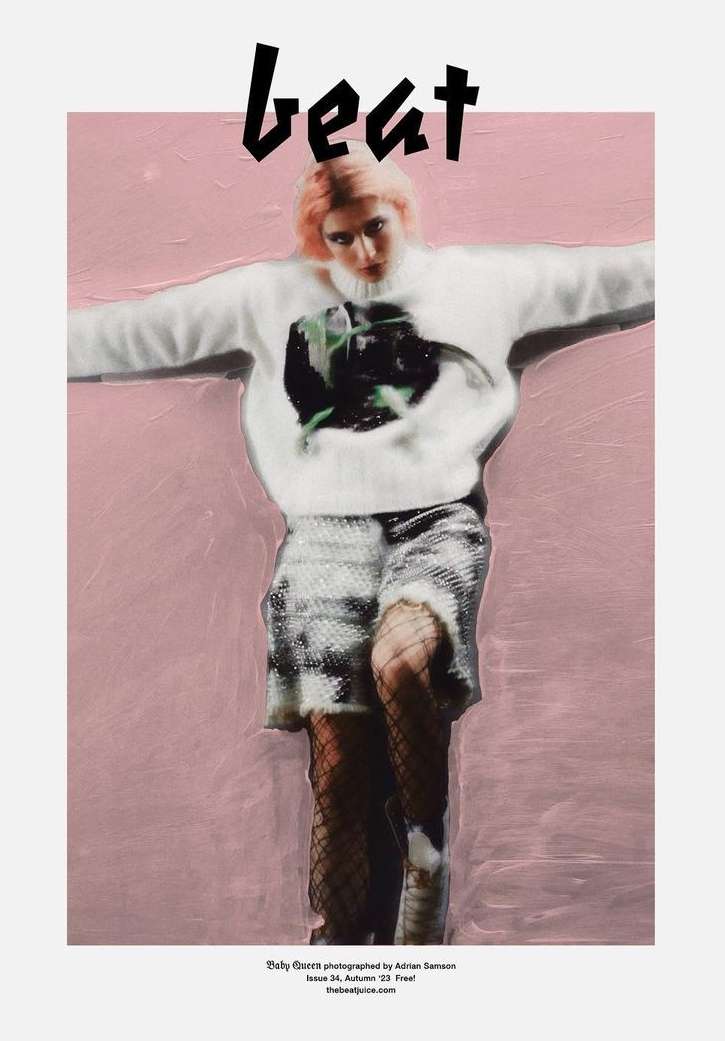 Editorial fashion shot of a pink-haired model wearing a printed sweater and sequined shorts against a pink backdrop.