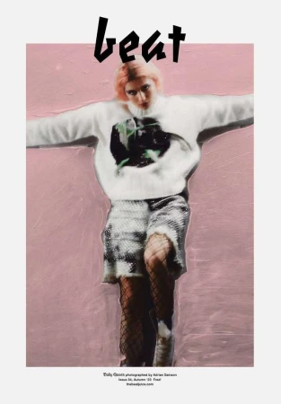Editorial fashion shot of a pink-haired model wearing a printed sweater and sequined shorts against a pink backdrop.