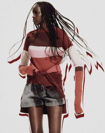 Black woman with long braided hair wearing a striped knit sweater and denim shorts against a white background