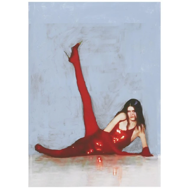 A woman poses while lying on the floor in a shiny red mini dress, red tights, and red high heels against a light blue background.