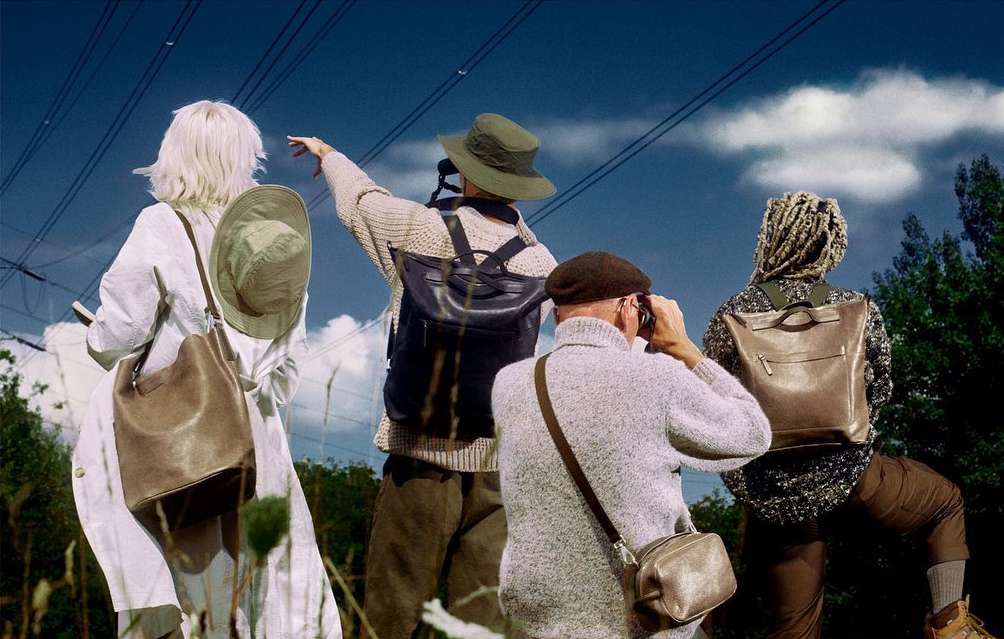 Four people seen from the back wearing backpacks, bucket hats and warm clothes, looking at the blue sky with clouds and power lines.