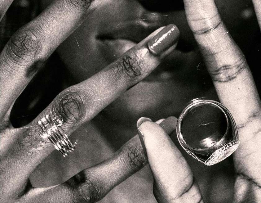 Close-up of an adult's hands with rings, showcasing jewelry on fingers, black and white tones, and well-manicured nails.