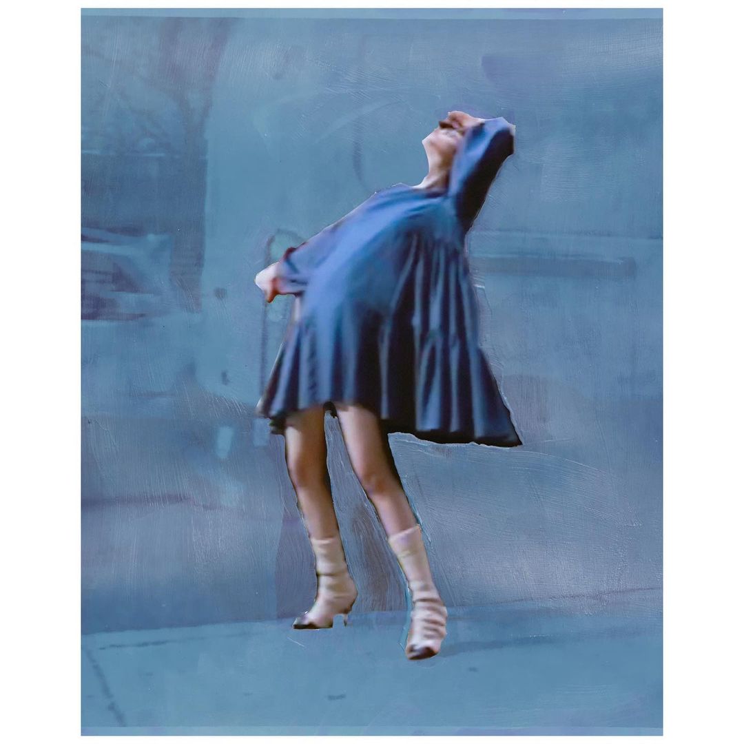 A woman with pale skin, wearing a blue dress and light-colored boots, stands with her head tilted back, captured against a muted blue background.