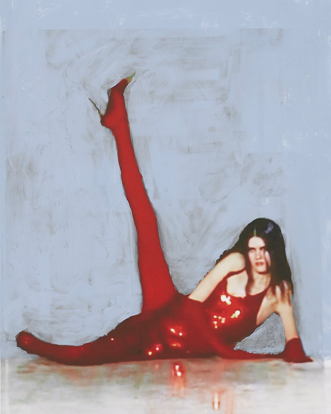 A model in a red, sparkling bodysuit and matching high heels strikes a pose, leg raised in an expressive manner, against a pale background.