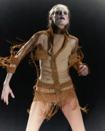 Model wearing a gold sequined fringe structured outfit against a dark background, photographed by Adrian Samson.