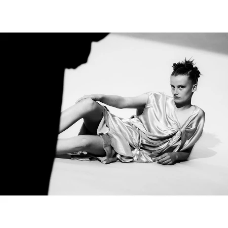 Model wearing a satin dress reclining on a white seamless backdrop, captured in black and white by Adrian Samson.