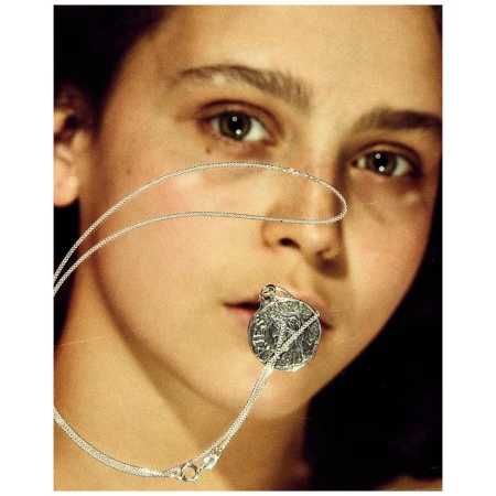 Close-up portrait of a woman wearing a silver chain necklace with a textured coin pendant held near her lips by photographer Adrian Samson.