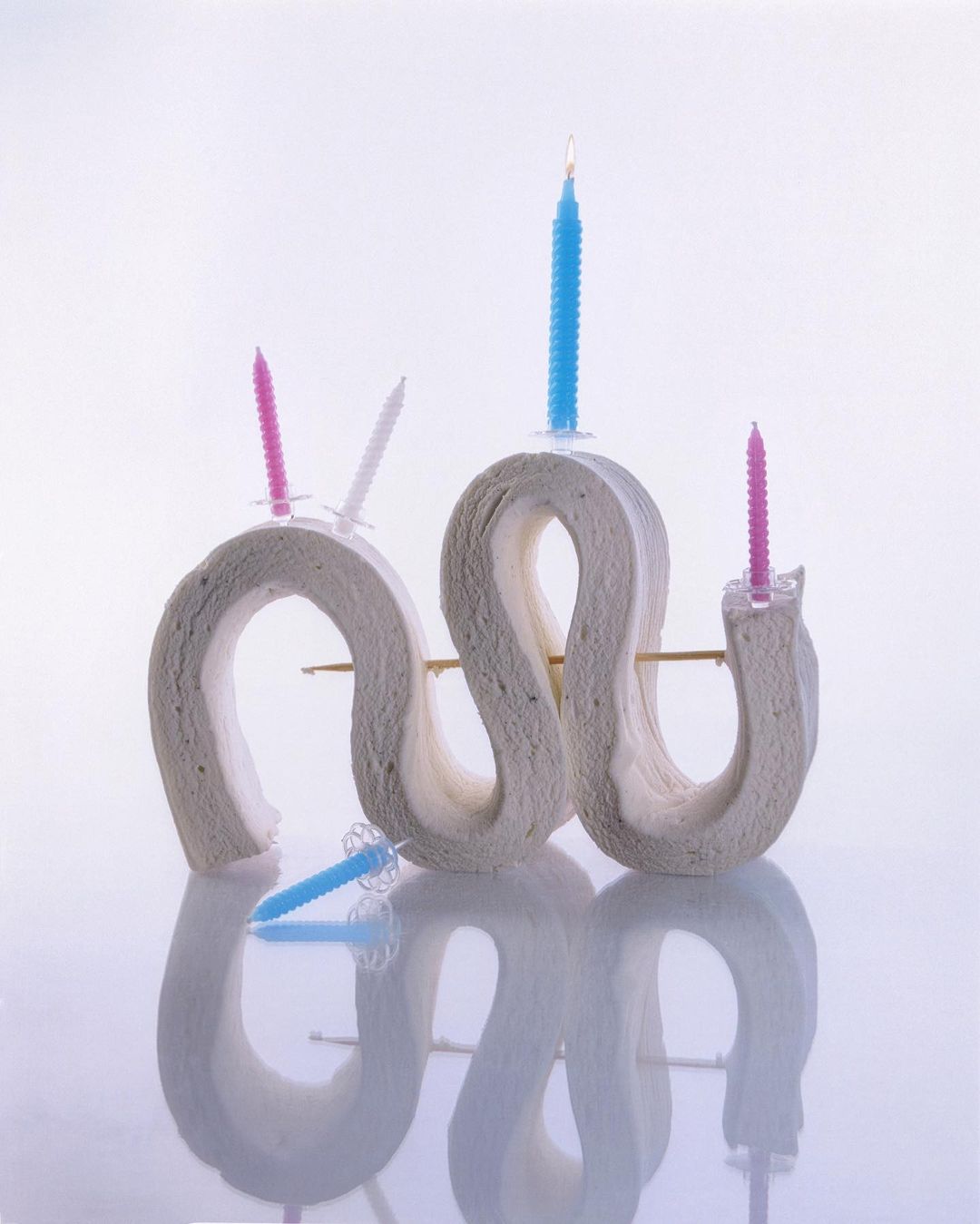 Abstract image featuring rolled paper candle holders with lit candles in white, blue, and pink hues against a soft white background.