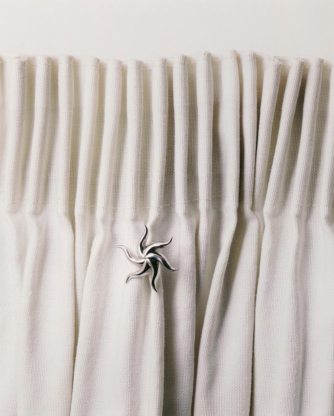 Close-up of draped white textile curtain with a silver ornamental holder, creating a serene and textured interior design detail.