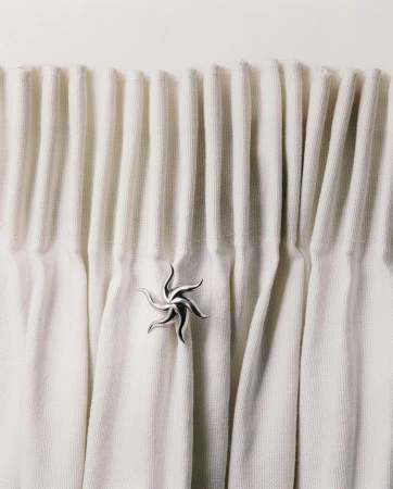 Close-up of draped white textile curtain with a silver ornamental holder, creating a serene and textured interior design detail.