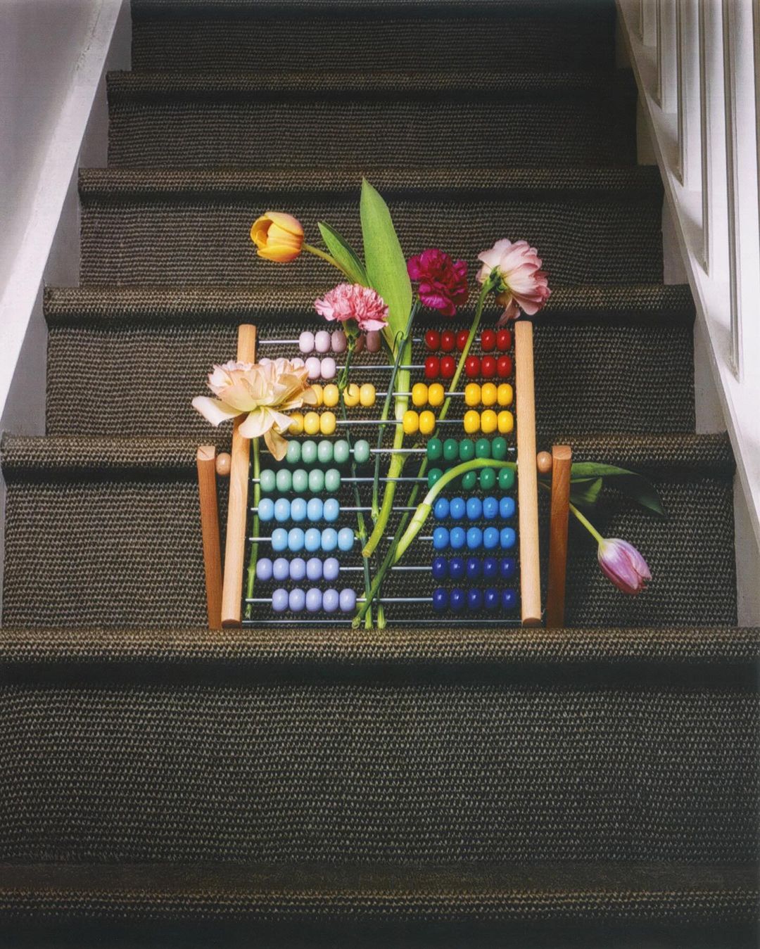 Still life of an abacus with colorful beads and flowers on a carpeted staircase, creating a playful, colorful, and unique composition.