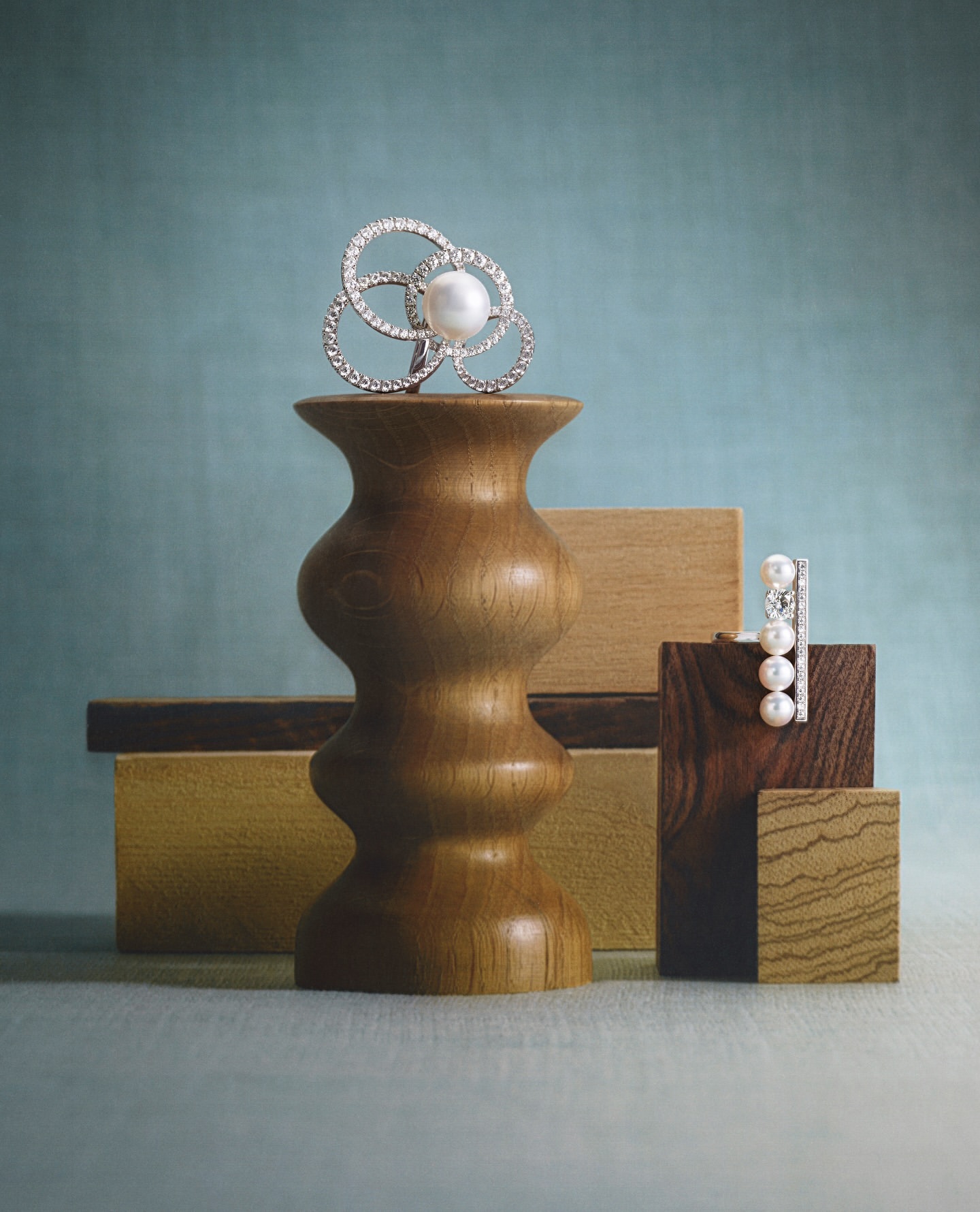 Elegant pearl and diamond jewelry displayed on wooden pedestals against a soft blue backdrop, emphasizing luxury and design.