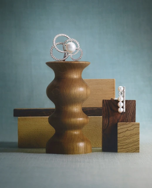Elegant pearl and diamond jewelry displayed on wooden pedestals against a soft blue backdrop, emphasizing luxury and design.