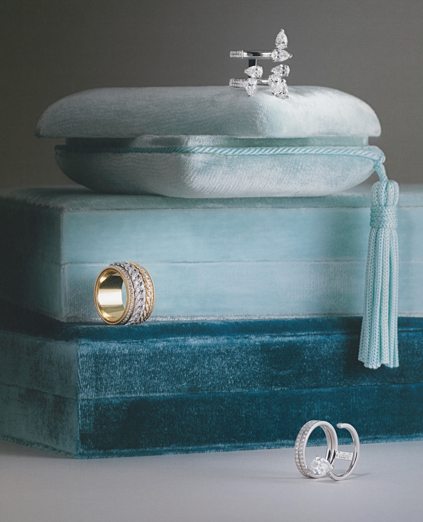 Stack of velvet jewelry display boxes showcases gold and silver rings in a studio setting with diffused light, creating an elegant presentation.