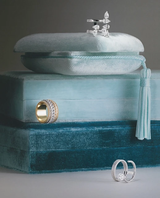 Stack of velvet jewelry display boxes showcases gold and silver rings in a studio setting with diffused light, creating an elegant presentation.