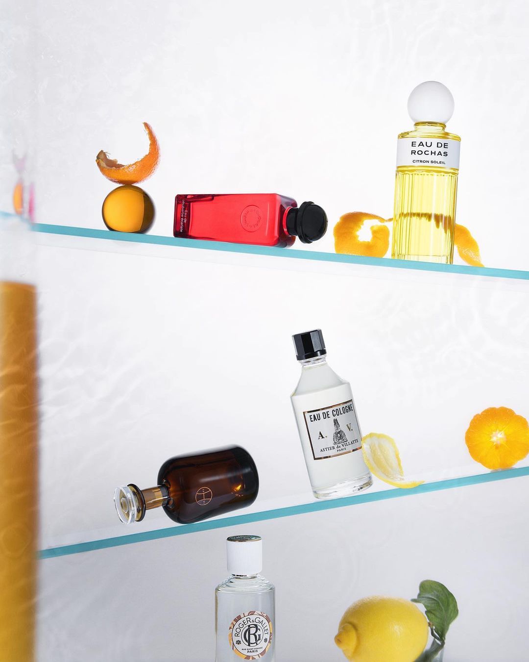 Still life studio shot of perfume bottles and citrus fruits on glass shelves, emphasizing beauty and minimalist composition.