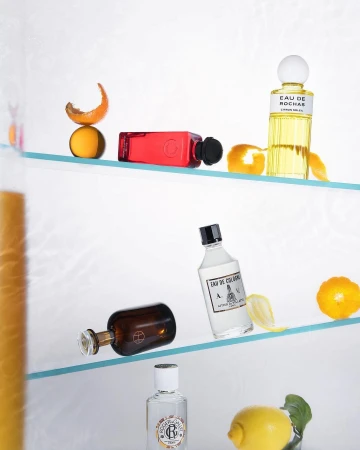 Still life studio shot of perfume bottles and citrus fruits on glass shelves, emphasizing beauty and minimalist composition.