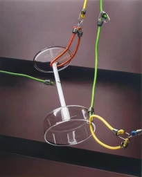 Clear glass objects suspended by colourful bungee cords and metal hooks against a dark brown structured background