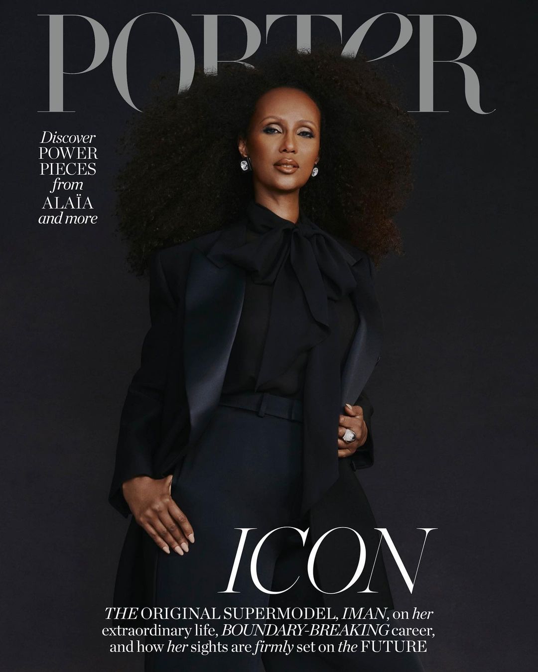 Magazine cover featuring Iman in black suit, large natural hair, diamond earrings and ring, standing against a solid dark backdrop.