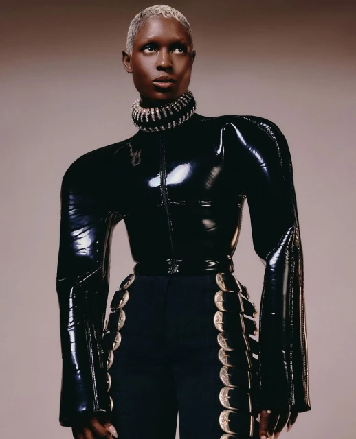 Elegant woman in black latex top and navy pants with silver accents in a fashion editorial shot against a neutral backdrop.