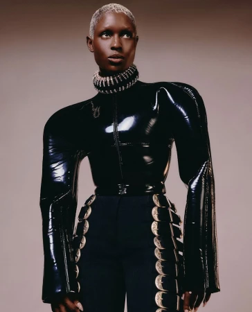 Elegant woman in black latex top and navy pants with silver accents in a fashion editorial shot against a neutral backdrop.