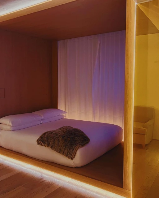 Bedroom interior featuring a platform bed with white linens and a brown throw, framed by a wooden structure with integrated lighting.