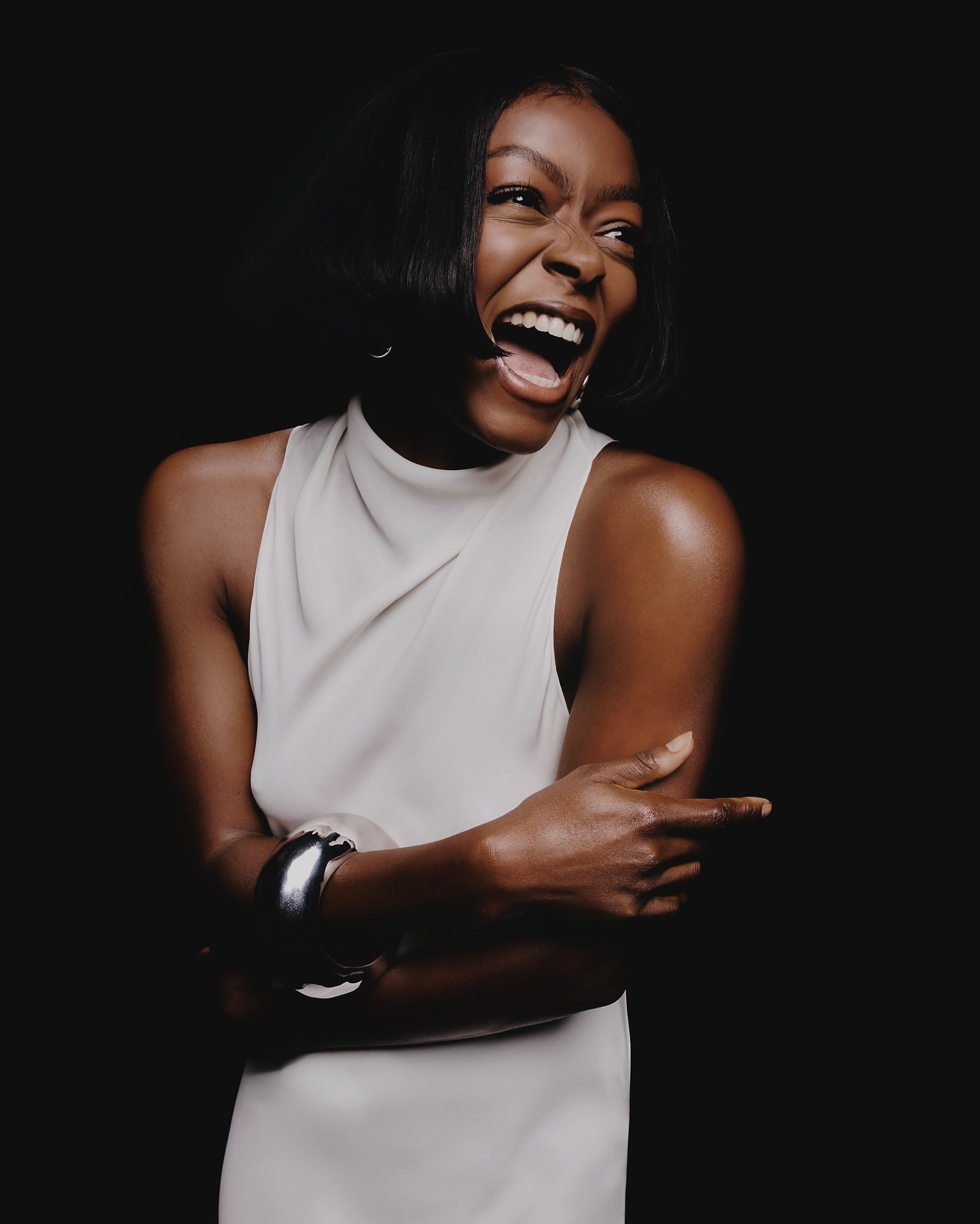 Smiling African-American woman in a sleeveless dress with a metal cuff bracelet, posing in front of a dark backdrop in a studio.