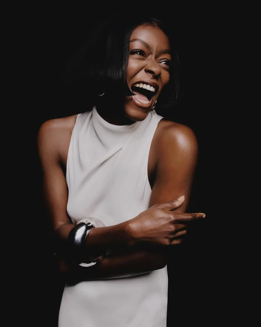 Smiling African-American woman in a sleeveless dress with a metal cuff bracelet, posing in front of a dark backdrop in a studio.