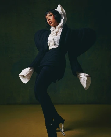 Woman in black sculptural jacket with exaggerated rounded shoulders and ruffled white blouse posing