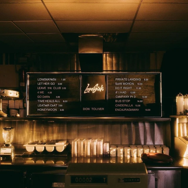 Close-up of a vintage-style menu board listing song titles, located inside what appears to be a diner or restaurant, warm lighting.