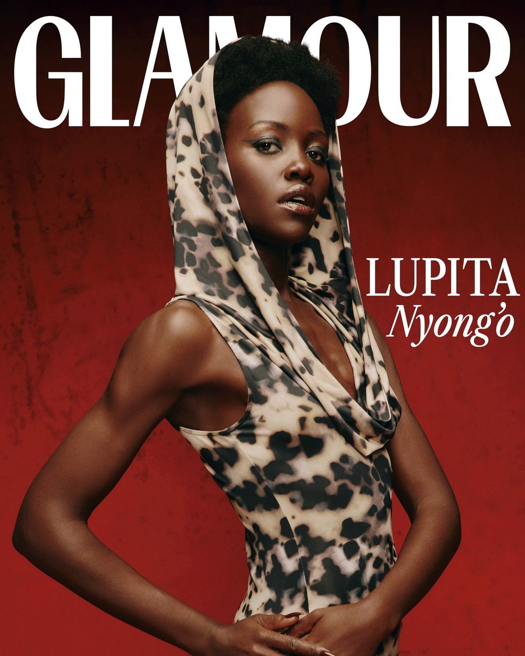 Glamour magazine cover featuring Lupita Nyong'o in a patterned hooded dress against a gradient red background with large white text.