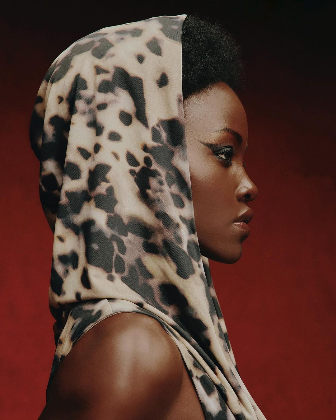 Profile portrait of an African American woman wearing a patterned scarf, set against a deep red background in a studio setting.
