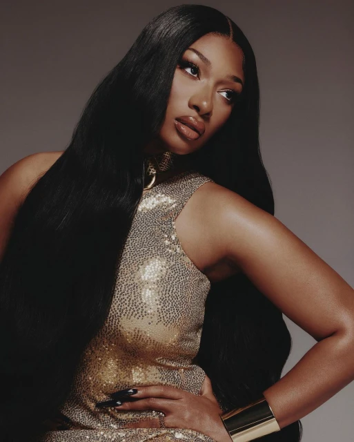 Portrait of a woman with long black hair, wearing a sequined dress, posing with her hand on her hip against a grey backdrop.