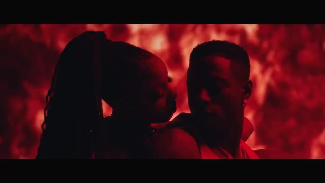 A man and a woman are silhouetted against a red background, possibly a promotional shot for music or entertainment content, casting shadows.