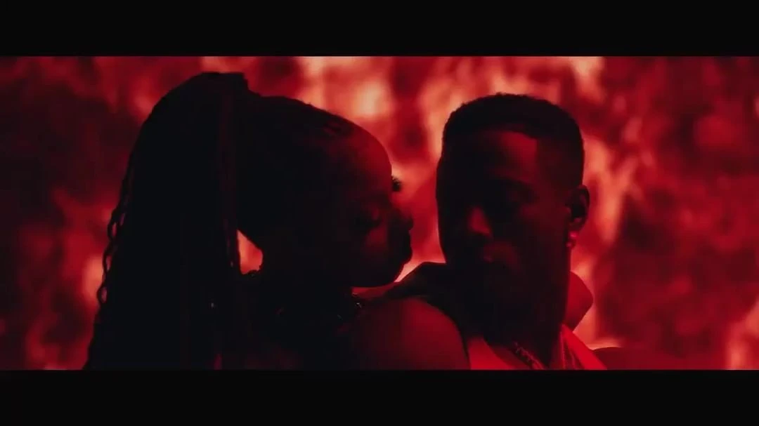 A man and a woman are silhouetted against a red background, possibly a promotional shot for music or entertainment content, casting shadows.