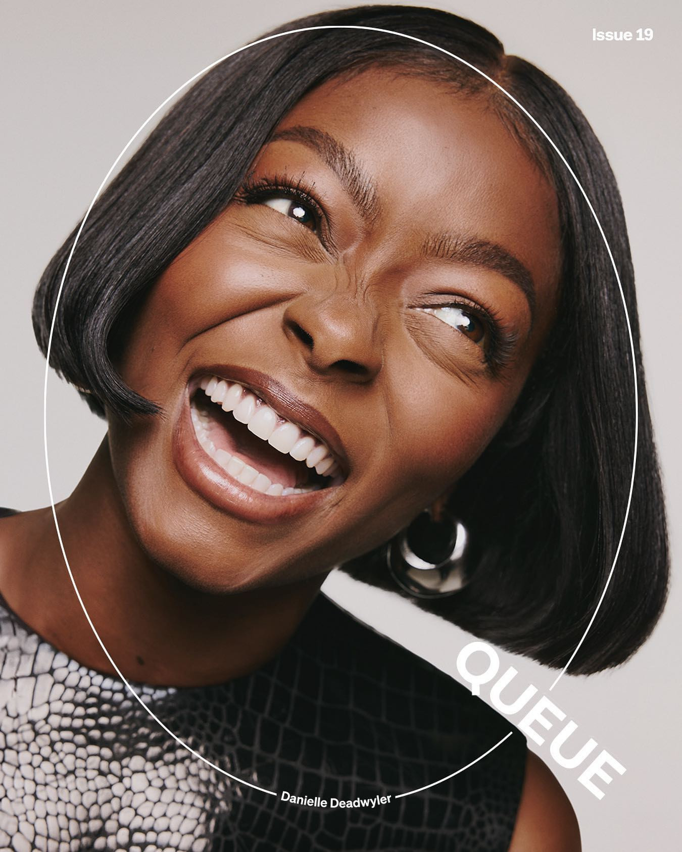 Close-up fashion cover portrait of a smiling African American woman with bob hairstyle, silver earrings, and snakeskin top. 