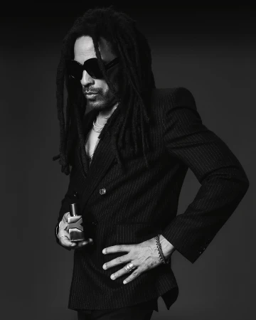Lenny Kravitz wearing a dark pinstripe blazer and sunglasses holding a fragrance bottle in a portrait by Adrienne Raquel