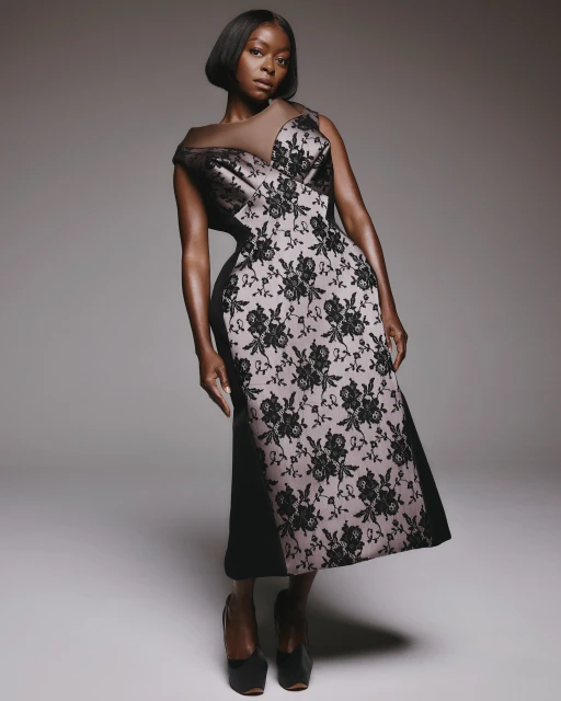 Elegant woman in a black and floral dress posing in a studio. She has a short bob haircut and wears dark heels.