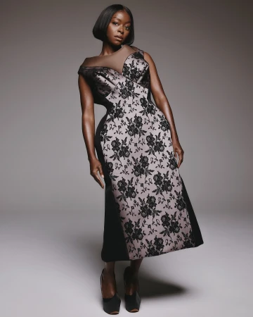Elegant woman in a black and floral dress posing in a studio. She has a short bob haircut and wears dark heels.