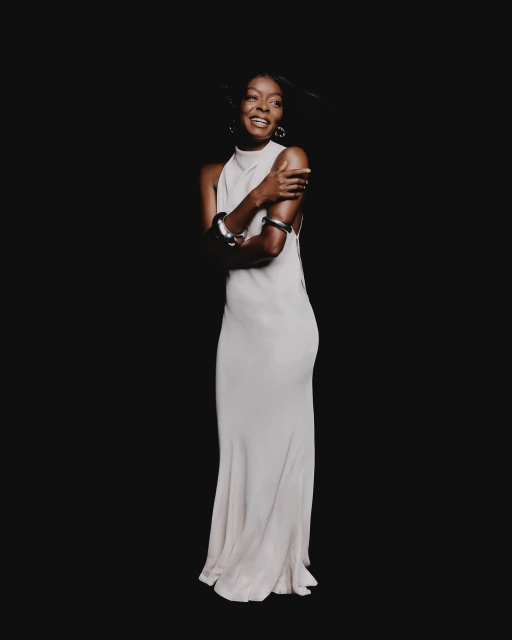 Elegant portrait of a smiling African-American woman in a light dress and silver bangles against a dark background, showcasing fashion and beauty.