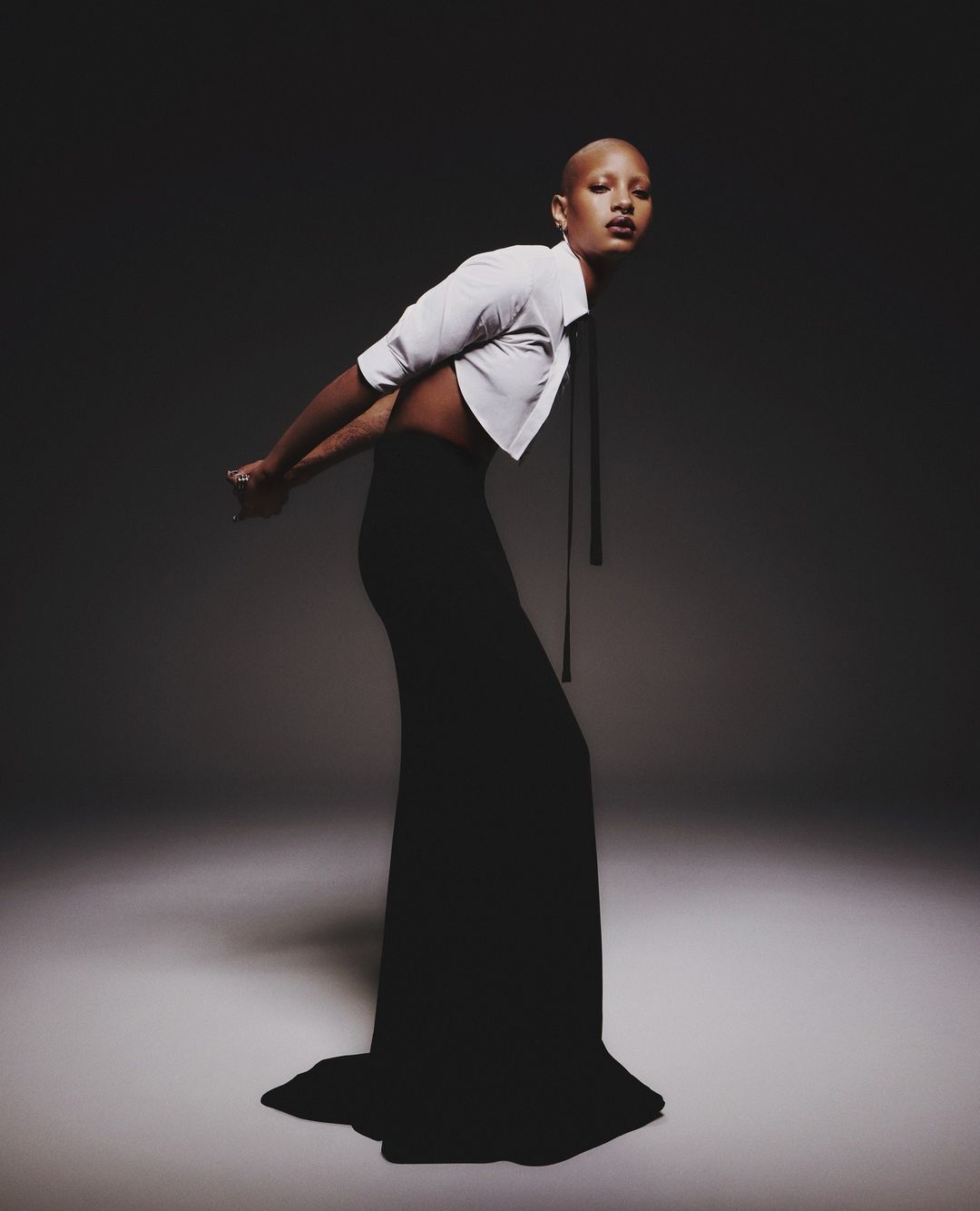 Fashion portrait of a woman with short hair, wearing a crop top and black skirt, posing in a dark studio with soft, diffused lighting.
