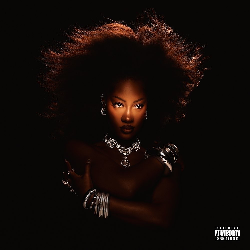 Portrait of a black woman with voluminous hair wearing diamond jewelry and silver bangles against a dark background.