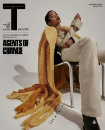Portrait of Laura Harrier seated on a metal chair wearing a tan jacket and trousers with a textured yellow throw, photographed by Adrienne Raquel.