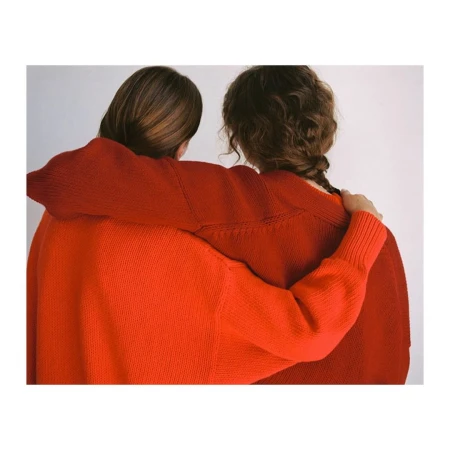 Two women with their arms around each other wearing red sweaters against a plain white background