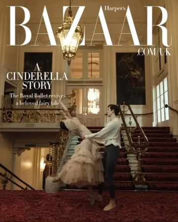 A couple of ballet dancers are posed on a staircase indoors in front of a large chandelier in an editorial fashion photograph.